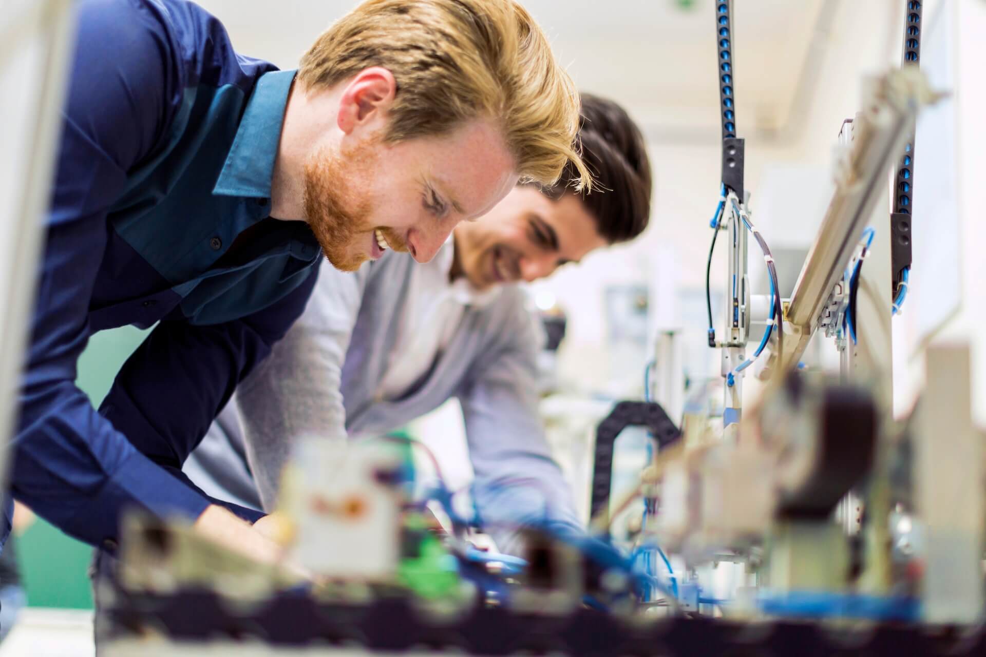 Two men operating a machine in a factory setting, focused on their tasks and surrounded by industrial equipment.